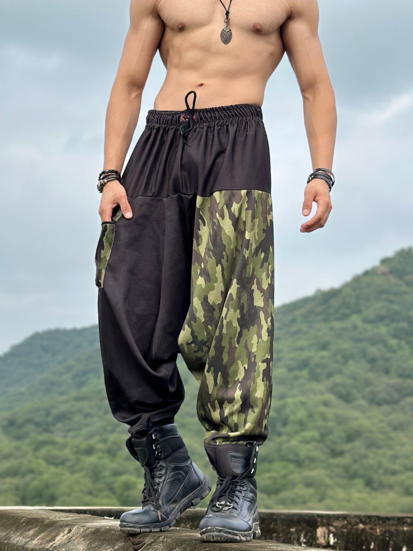 A man standing on a elevated road wearing camouflage military camo harem print harem pants with an elastic waistband and drawstrings.