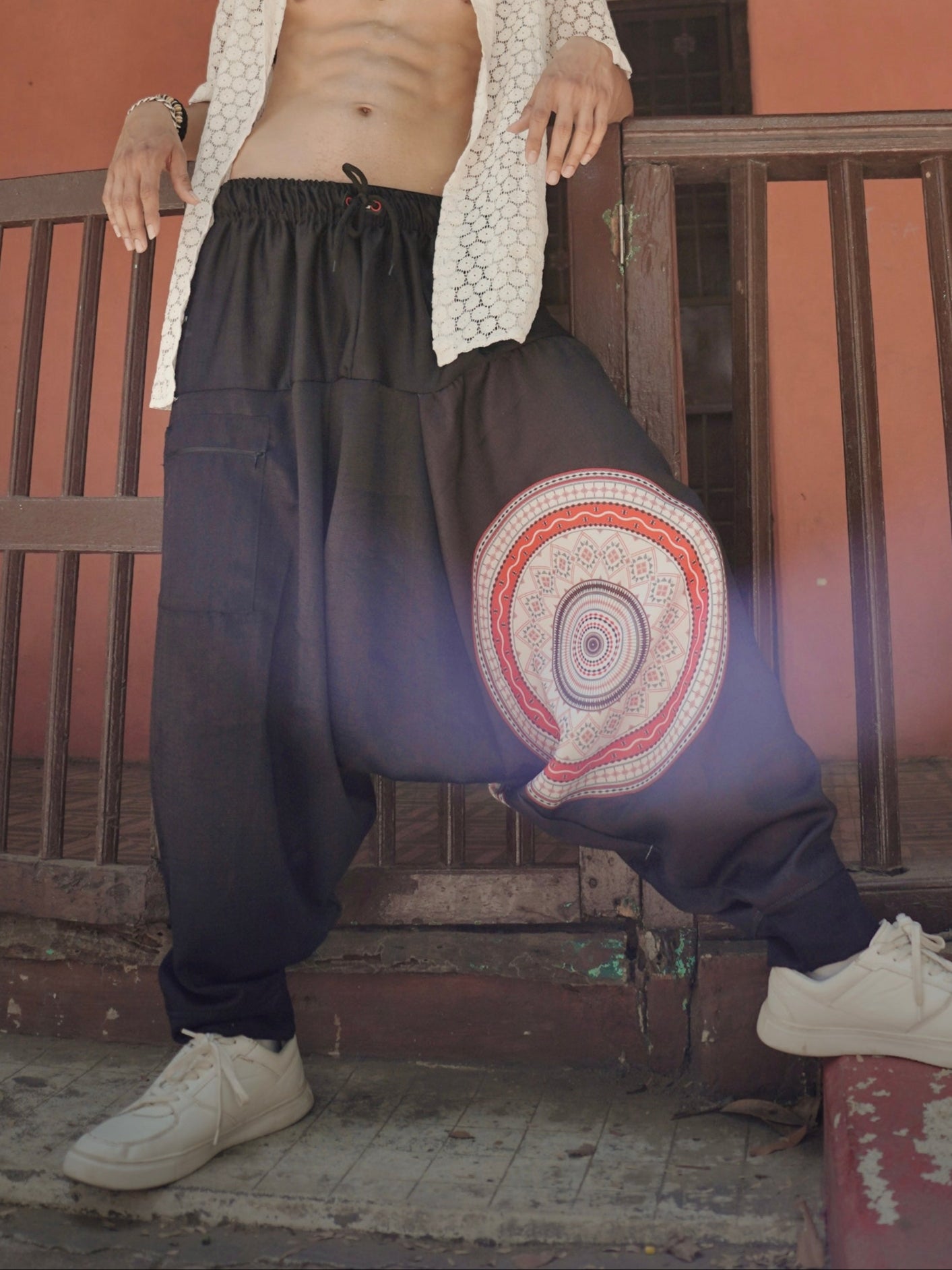 Man wearing a loose-fitting outfit with a colorful patterned pants in front of a rustic building.