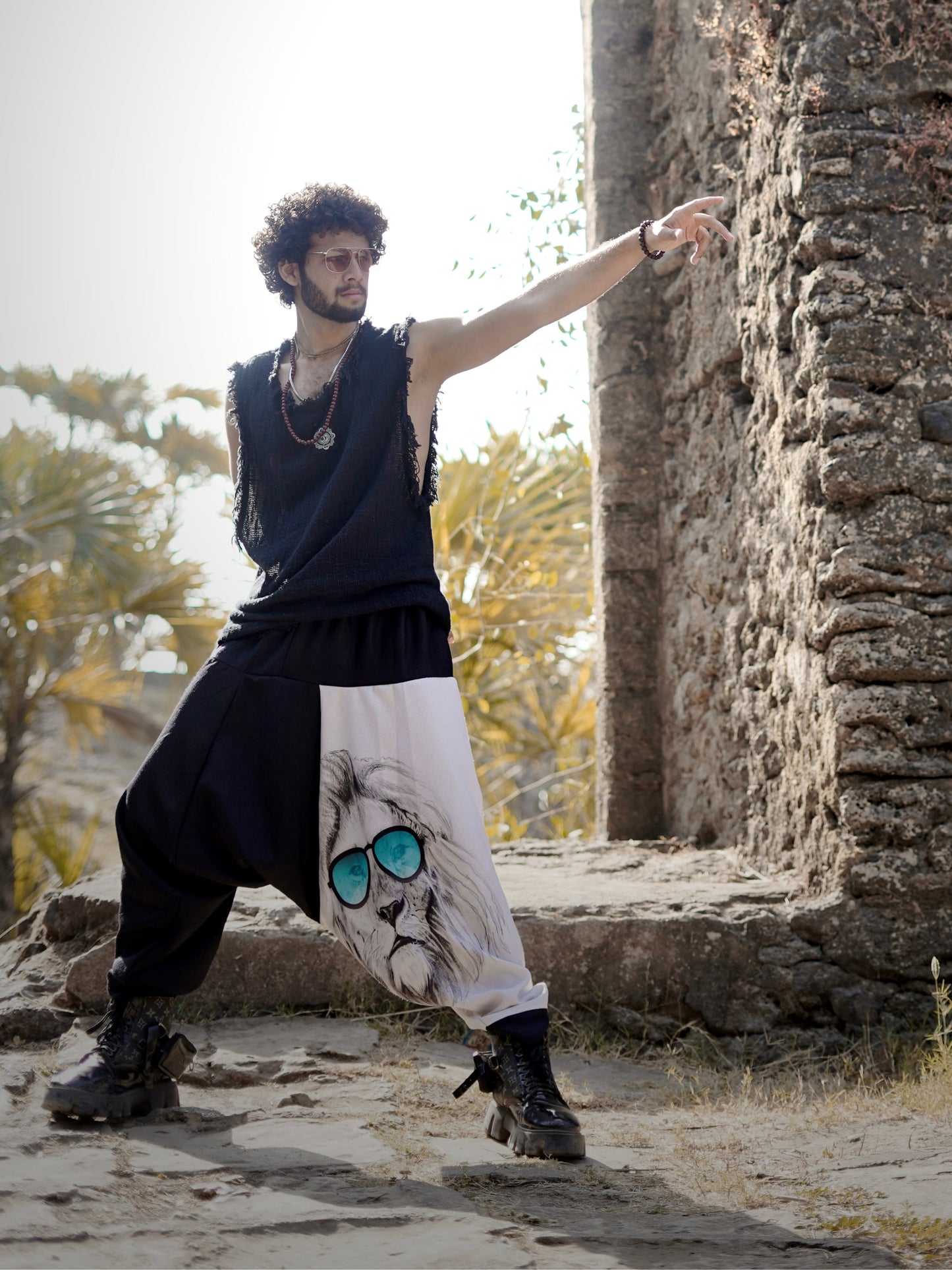 Man wearing a harem pants with a lion design, standing outdoors near stone ruins.