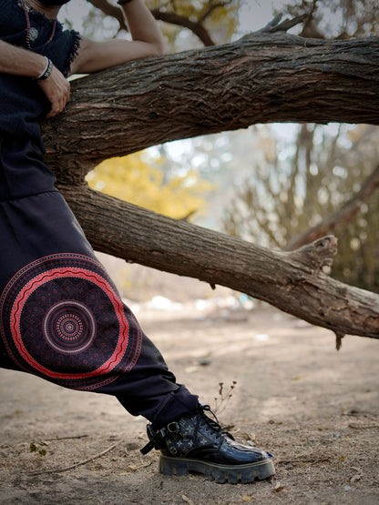 Person wearing dark pants with a red and purple circular design, standing next to a tree in a natural setting.